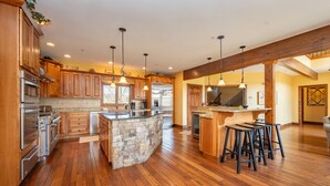 A spacious kitchen with wooden cabinets, a central island, and a bar area with stools. - Luxury Lake Escape w/ Indoor Pool & Hot Tubs (Swanton)