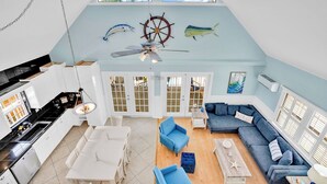 A spacious loft with a kitchen, dining area, and living room. It features a high ceiling, large windows, and nautical-themed wall art. - P78 - Charming 3 bedroom 2 bath home in Sombrero Beach with dock and pool (Marathon)
