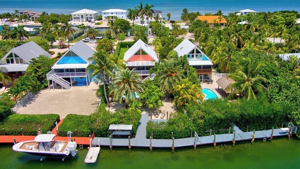 A coastal resort with multiple bungalow-style buildings, a swimming pool, and a dock with a boat. - P78 - Charming 3 bedroom 2 bath home in Sombrero Beach with dock and pool (Marathon)