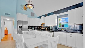 A modern kitchen with white cabinetry, a central island, and a dining area with white chairs. - P78 - Charming 3 bedroom 2 bath home in Sombrero Beach with dock and pool (Marathon)