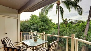 Un balcone con tavolo in vetro e sedie a righe, immerso nel verde rigoglioso e palme.