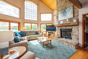 A spacious living room with a stone fireplace, large windows, and a cozy seating area.