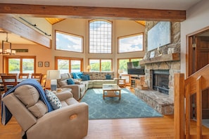 A spacious living room with a stone fireplace, large windows, and a cozy seating area.