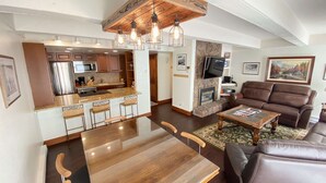 Una cocina moderna con una isla central, un comedor con mesa de vidrio y una sala de estar con sofá de cuero y chimenea.