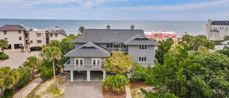 A coastal residential area with a two-story house featuring a covered front porch and a driveway leading to the entrance.