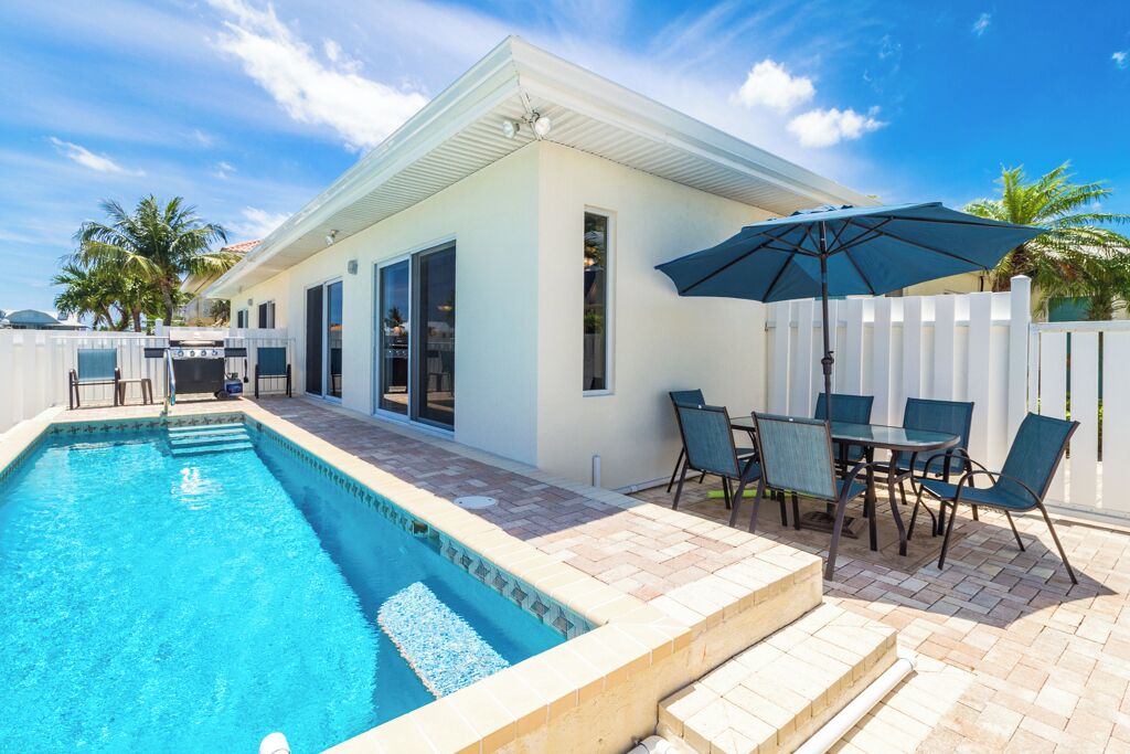 A swimming pool with a patio area, outdoor seating, and a white fence.