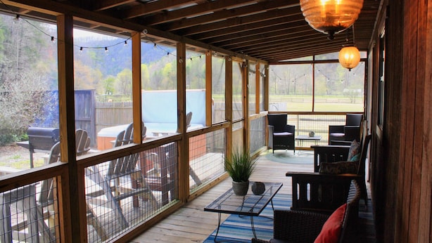 Eine überdachte Terrasse mit Holzboden, Gartenmöbeln und Blick auf einen See.