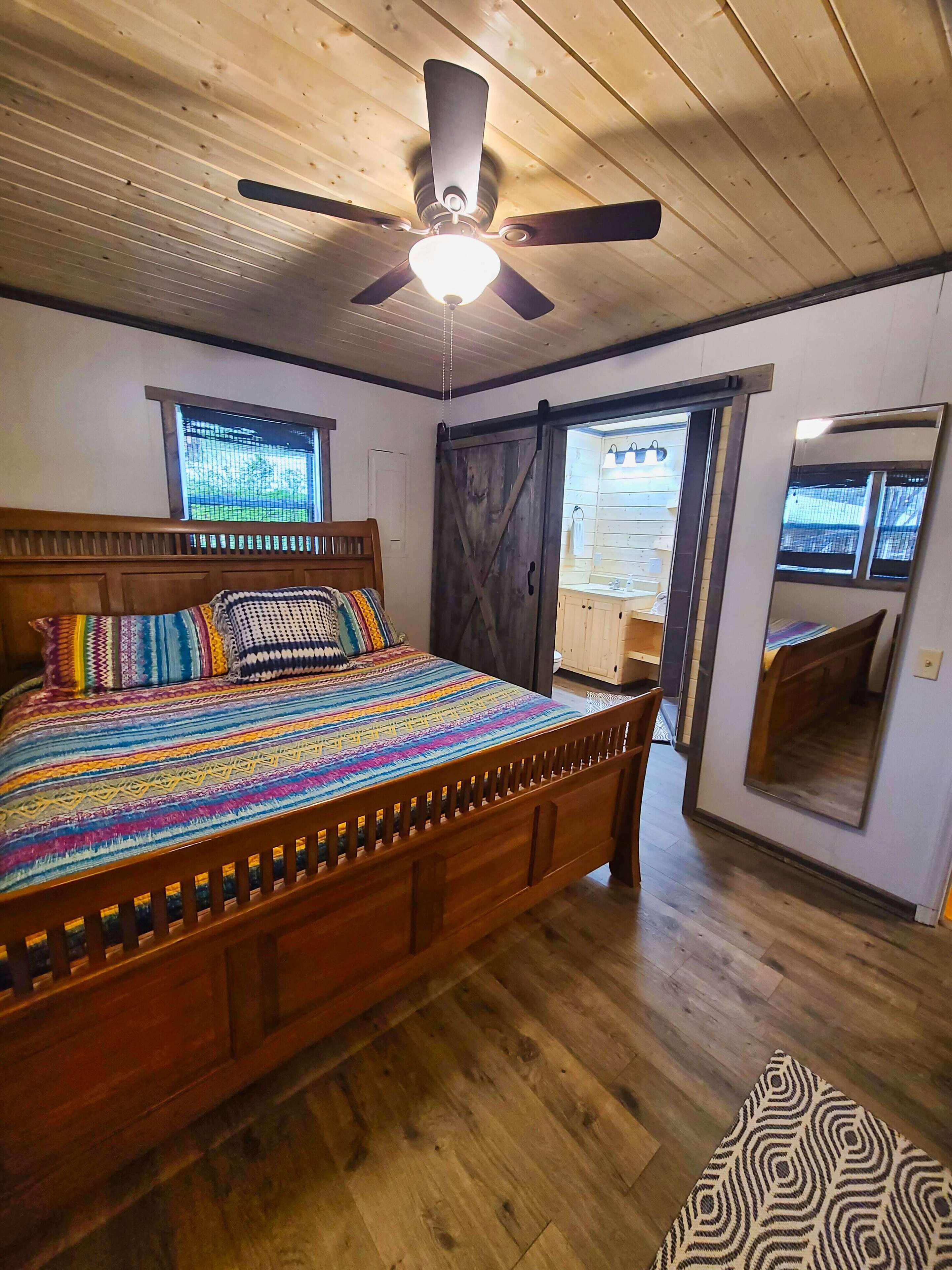 A bedroom with a wooden bed, a ceiling fan, and a large mirror.