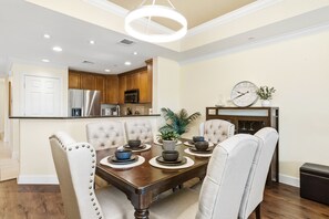 A dining area with a wooden table, cushioned chairs, and a modern kitchen in the background. - Beautiful Modern Condo with Private Balcony and Golf Course Views (Four Corners)