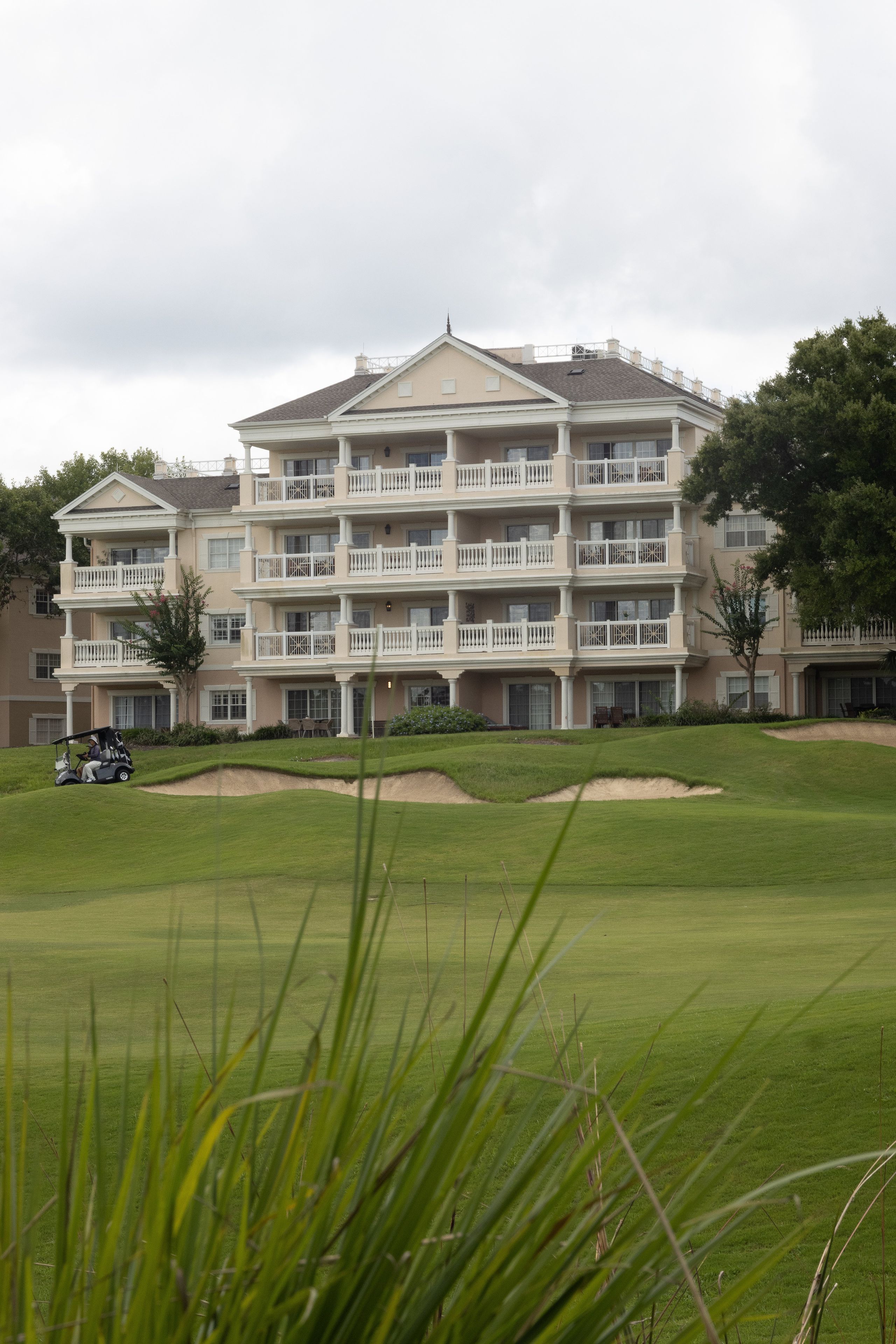 A multi-story hotel with balconies, a golf course in the foreground, and a cloudy sky.
