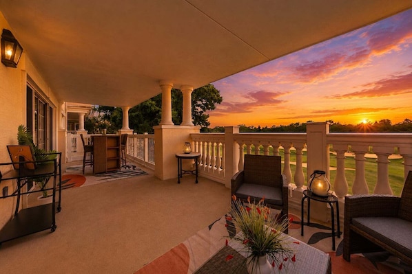 Un espace extérieur abrité, avec des chaises et des tables, d’où l’on peut admirer un coucher de soleil, et un terrain de golf en arrière-plan.