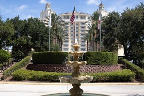 A fountain with multiple tiers in front of a building with two towers and flags.