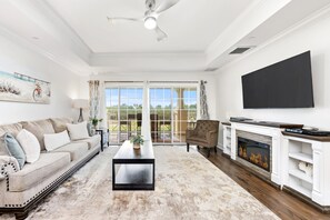 A living room with a sofa, armchair, coffee table, fireplace, TV, and large windows. - Beautiful Modern Condo with Private Balcony and Golf Course Views (Four Corners)