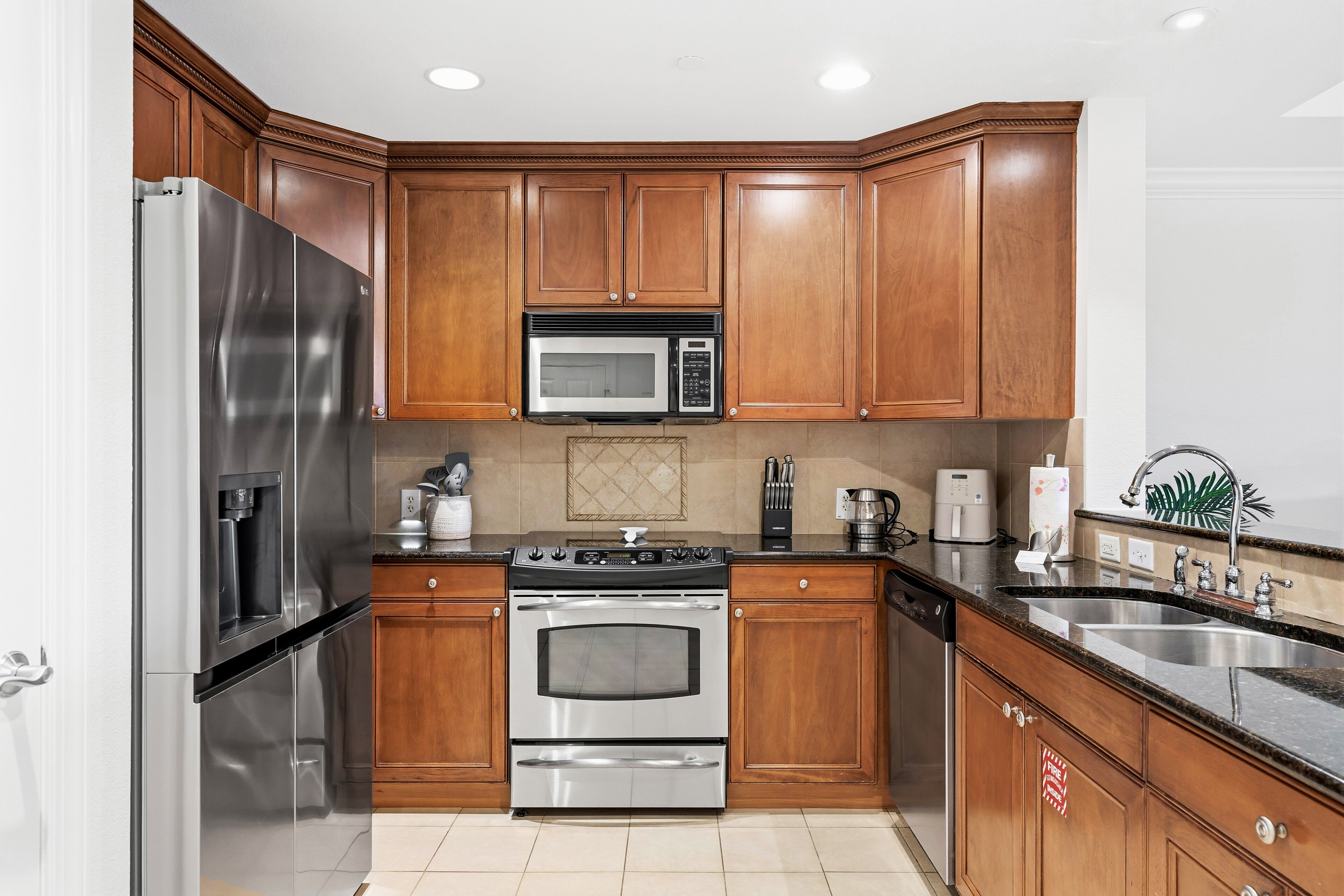 A modern kitchen with stainless steel appliances, wooden cabinetry, and a granite countertop.