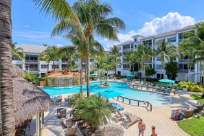A resort with a swimming pool, lounge chairs, palm trees, and a thatched-roof structure. - Beautiful 2 Bedroom with Pool View! (Bonita Springs)