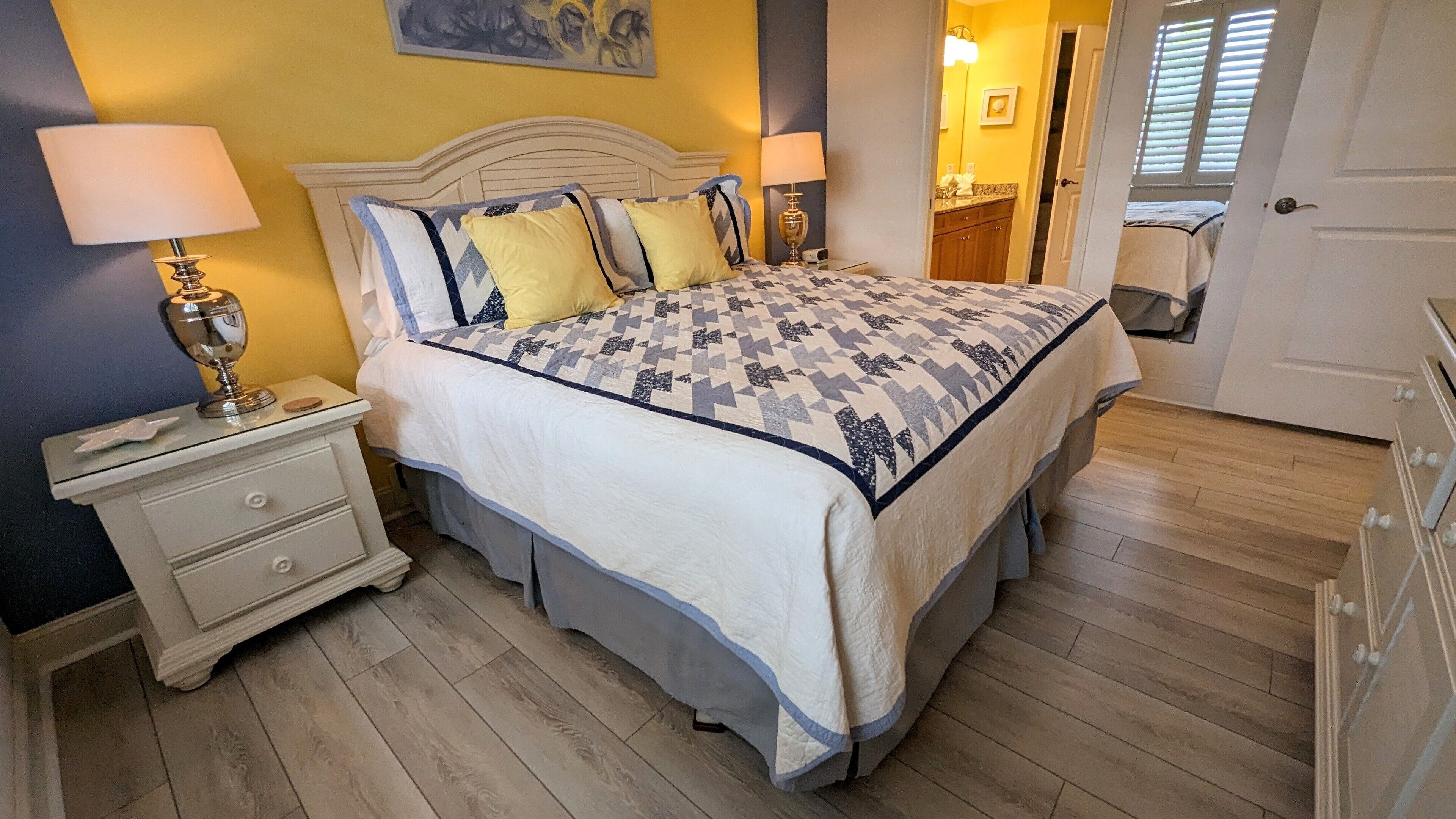 A bedroom with a bed, nightstands, a lamp, and a wooden floor.