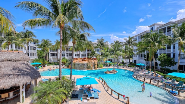 Ein Resort mit Schwimmbad, Liegestühlen, Palmen und einem strohgedeckten Gebäude.