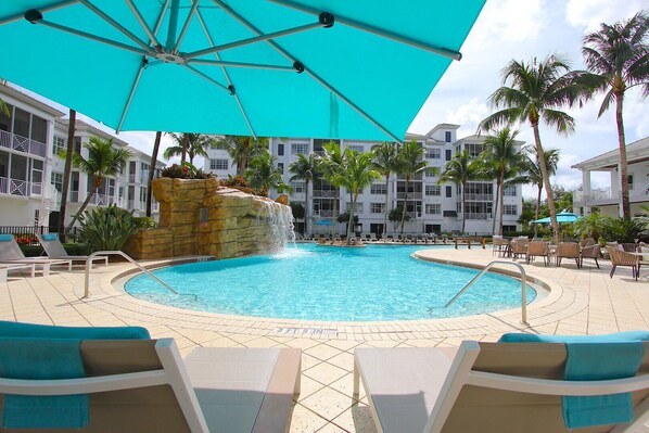 A pool area with lounge chairs, a turquoise umbrella, and a waterfall feature. - Relax In This Poolside Paradise! (Bonita Springs)