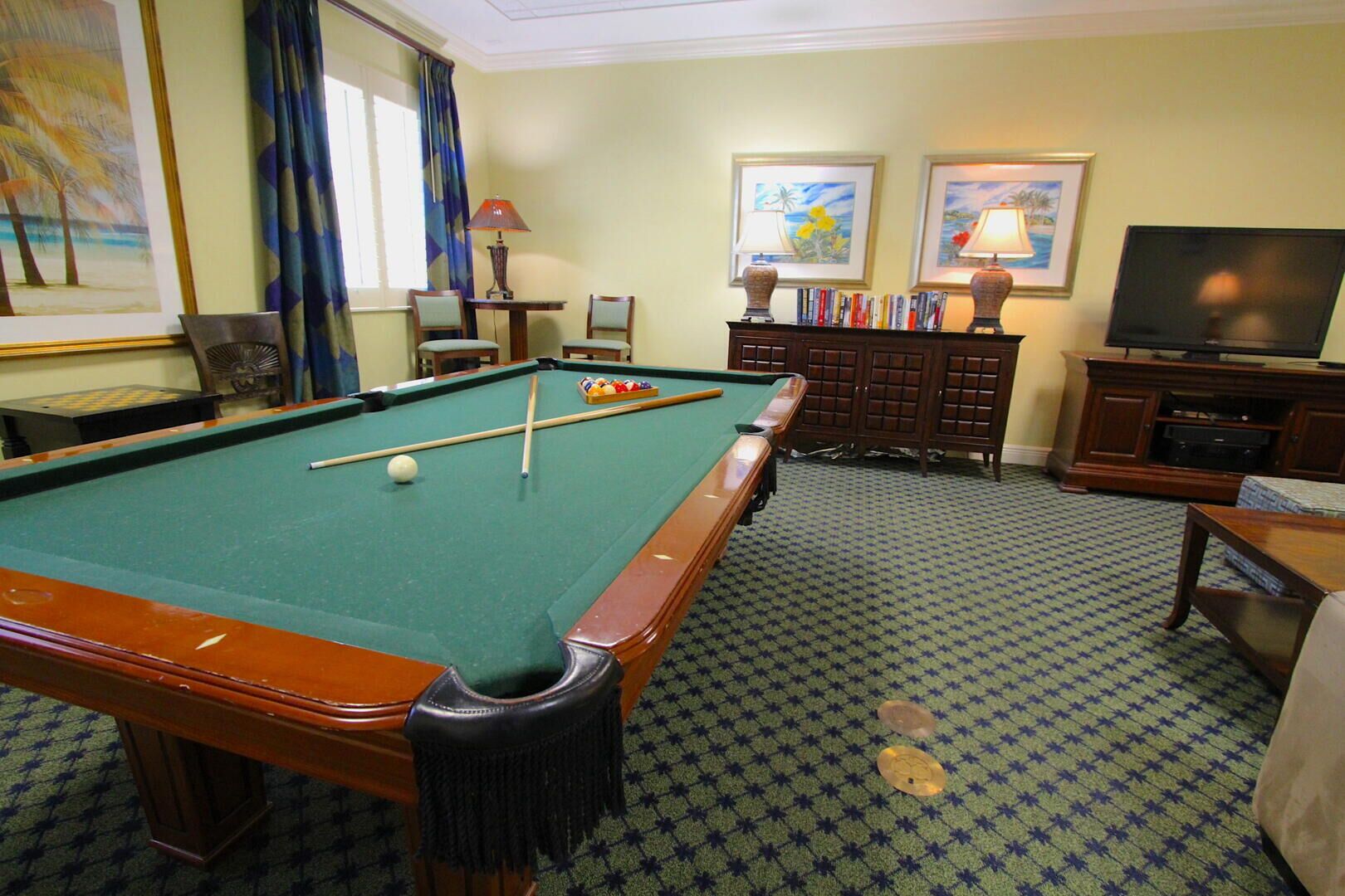 A pool table with balls, a television, and framed artwork on the walls.