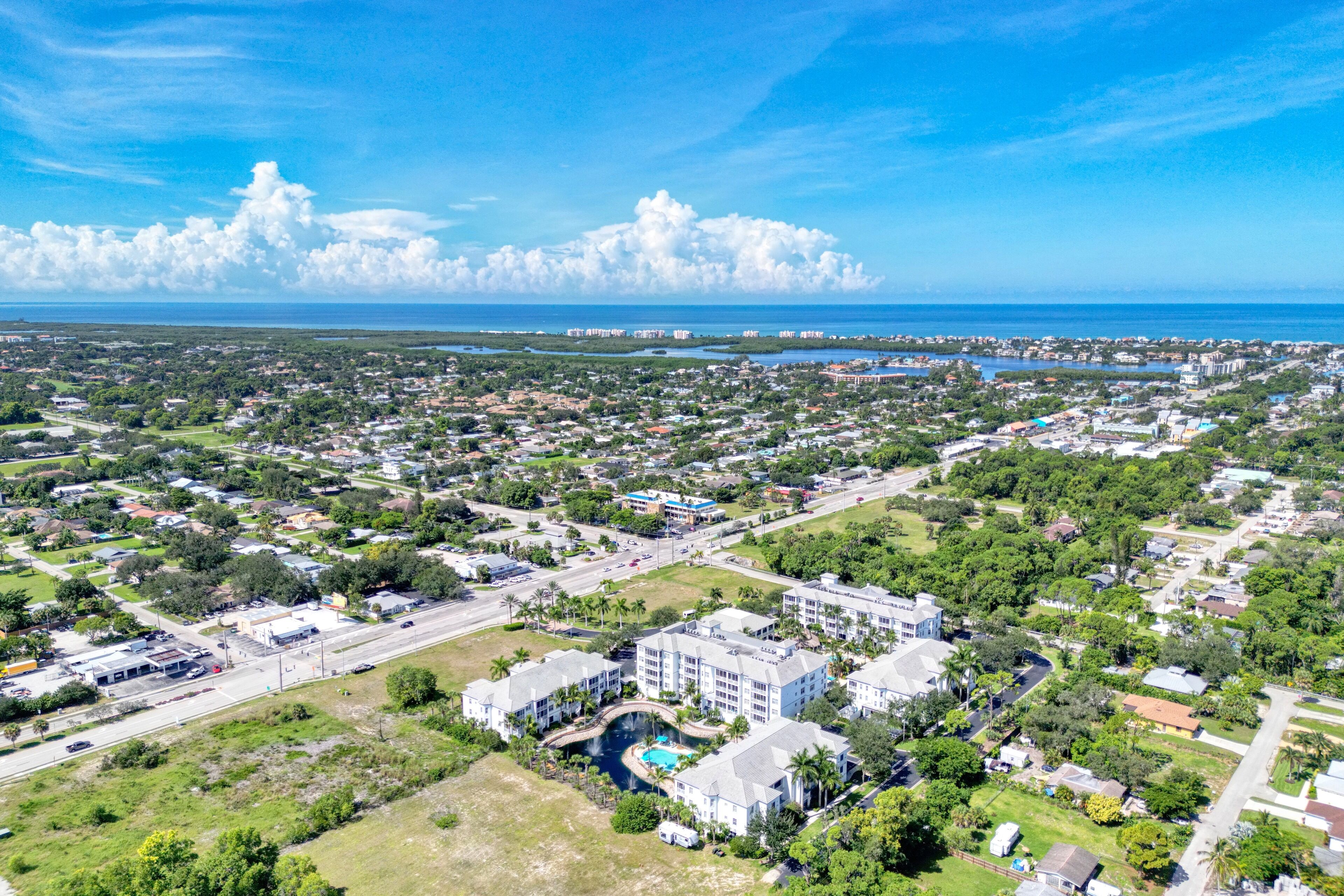 An aerial view of a coastal town with a marina, residential areas, and a large hotel with multiple floors and a swimming pool.