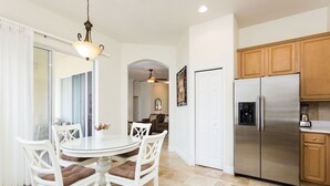 A dining area with a round table and white chairs, a kitchen with wooden cabinets and stainless steel appliances, and a ceiling fan.