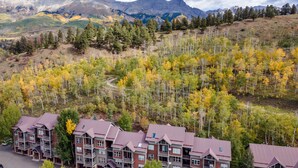 Un hotel de varios pisos con techo rojo, rodeado de follaje otoñal y montañas al fondo.