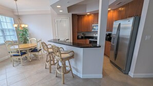Une cuisine moderne dotée d’un îlot central, de meubles en bois, d’appareils électroménagers en acier inoxydable et d’un coin repas avec des chaises en osier.