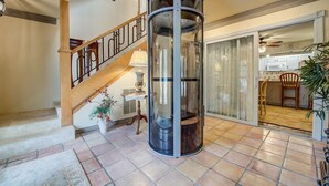A spacious living area with a wooden staircase, a glass elevator, and a sliding glass door leading to a kitchen. - Second Row, Steps away from the Ocean, Pool Table, Large Sun Deck (Georgetown)