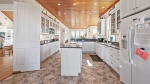 Une cuisine spacieuse avec des meubles blancs, un îlot central et un plafond en bois.