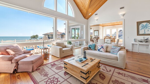 Un vaste salon doté d’une grande fenêtre donnant sur la mer, d’un plafond en bois et d’un coin salon confortable avec une table basse.
