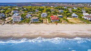 Vue aérienne d’une zone résidentielle côtière, avec des maisons, une plage et des vagues de l’océan.