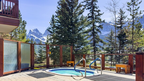 A pool area with a hot tub, surrounded by wooden deck and a view of snow-capped mountains. - Adorable mountain studio  (Canmore)