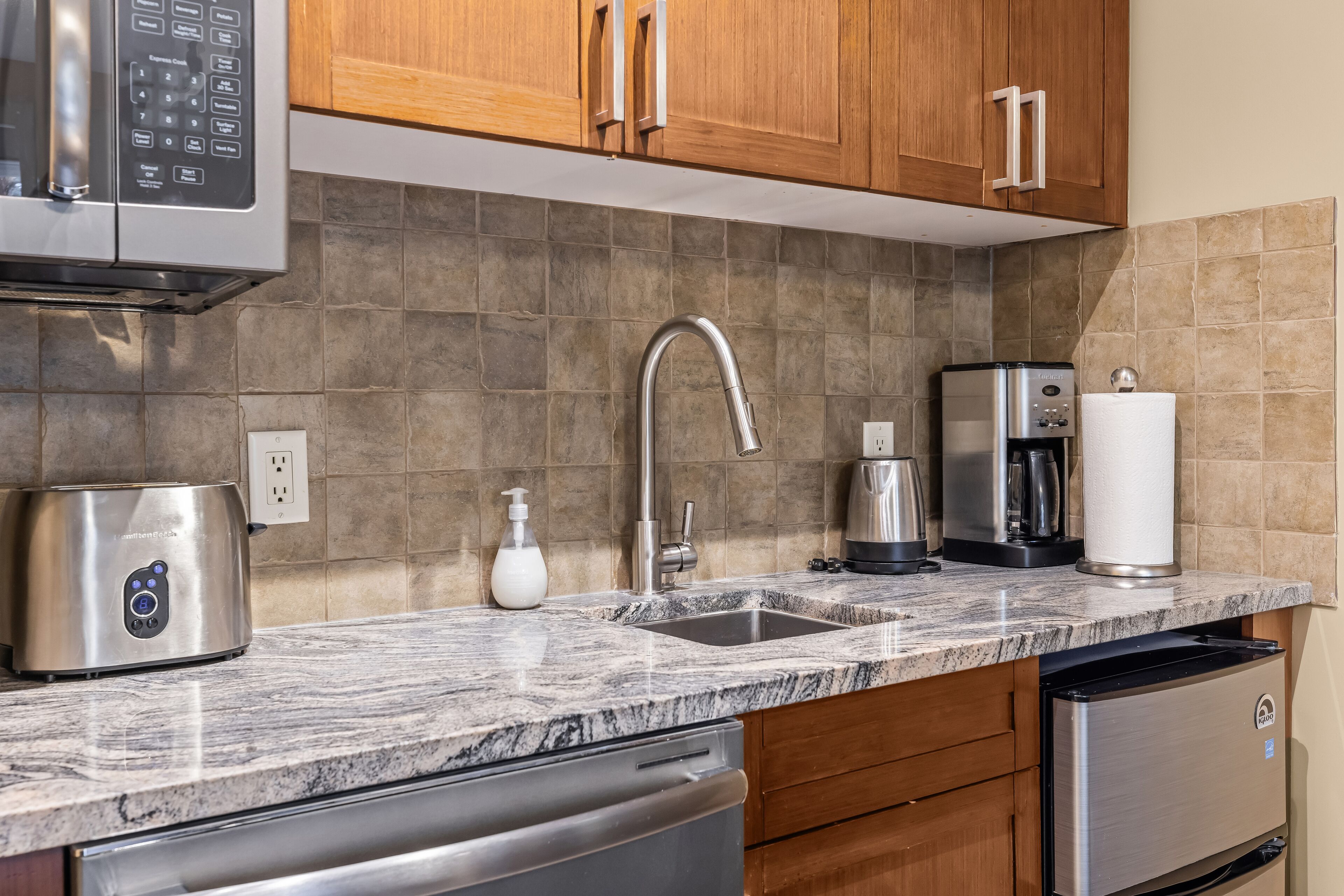 A kitchen with a stainless steel dishwasher, a coffee maker, a toaster, and a sink with a faucet.