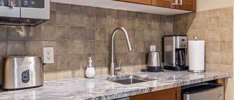A kitchen with a stainless steel dishwasher, a coffee maker, a toaster, and a sink with a faucet.