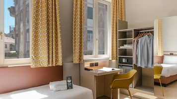 Habitación de hotel con cama, escritorio, silla, armario y vistas a la ciudad.
