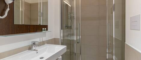 A modern bathroom with a glass-enclosed shower, a white sink, and a hairdryer mounted on the wall.