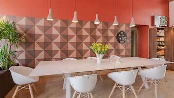Ein moderner Essbereich mit Wand in geometrischem Muster, einem langen Tisch, weißen Stühlen und hängenden Pendelleuchten.