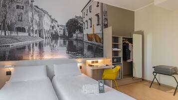 Ett hotellrum med två sängar, ett skrivbord, en stol, en garderob och en stor väggmålning som föreställer en kanalvy.