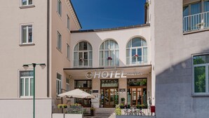 A hotel entrance with a sign reading "HOTEL TREVISO," featuring large arched windows, a covered outdoor seating area, and a bicycle parked outside. - B&B Hotel Treviso (Treviso)