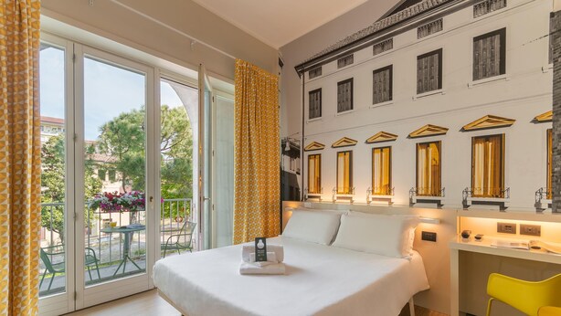 A hotel room with a bed, a desk, and a balcony with yellow curtains. - B&B Hotel Treviso (Treviso)