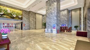 A spacious lobby with marble flooring, a reception desk, and a large mural of birds on the wall.