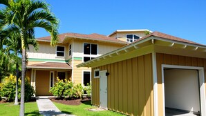A two-story house with a garage, a front yard with a palm tree, and a pathway leading to the entrance. - Beautiful Townhome with Exquisite Furnishings.  Garage available for guest use. (Kailua - Kona)