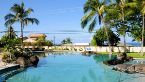 A clear blue pool with rocks, palm trees, and a view of the ocean. - Beautiful Townhome with Exquisite Furnishings.  Garage available for guest use. (Kailua - Kona)