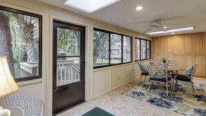 A sunlit room with a dining area, large windows, and a ceiling fan.