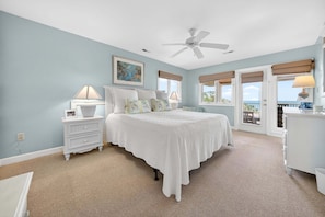 A bedroom with a bed, nightstands, a ceiling fan, and a view through the window.