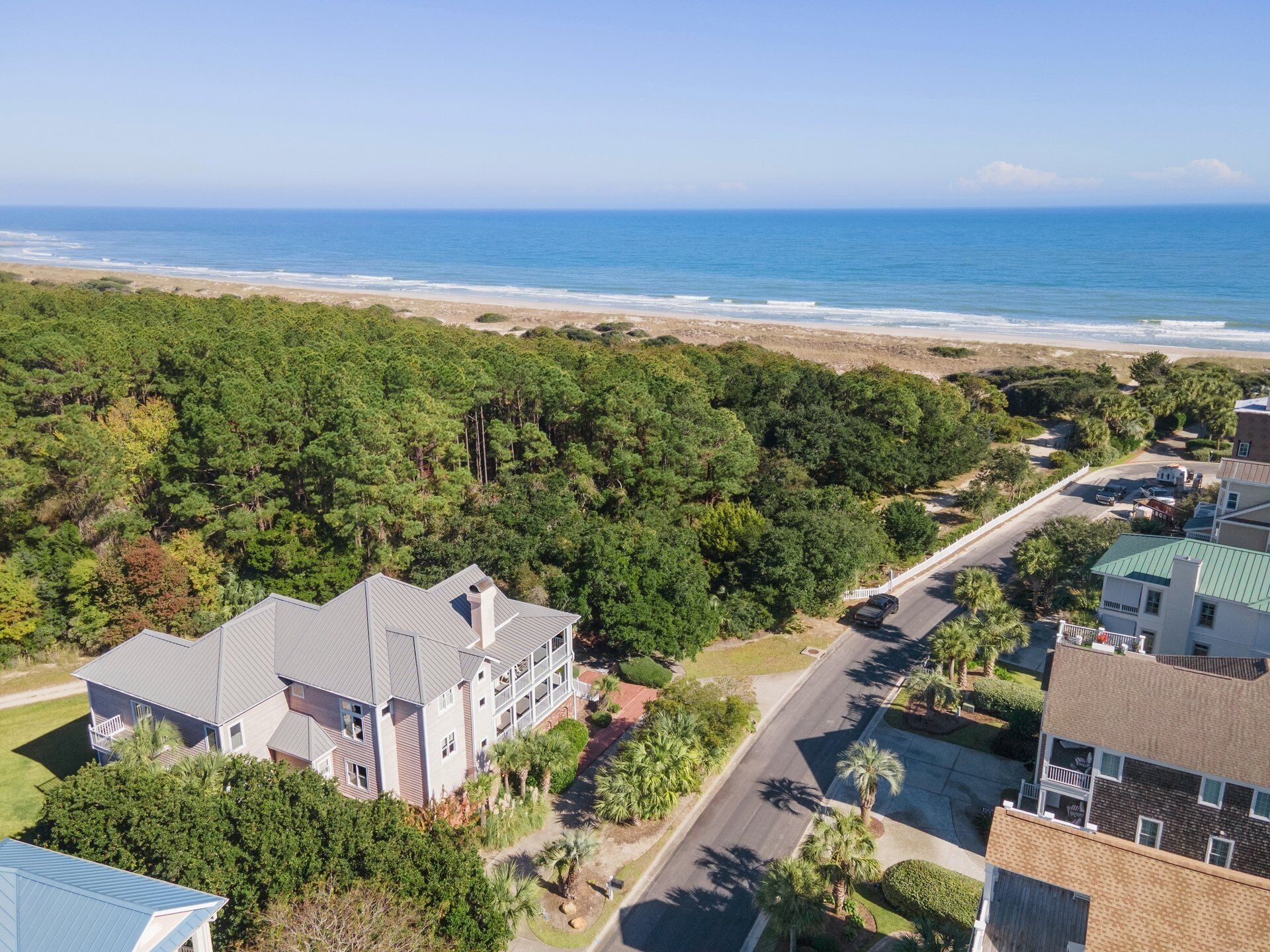 An aerial view of a coastal residential area with houses, a road, and a beach.