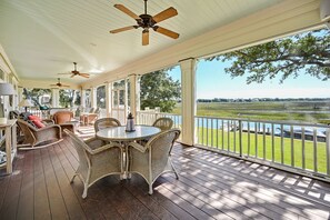A covered porch with wicker furniture, a round table, and a view of a water body. - Secluded Creekfront Home (Georgetown)