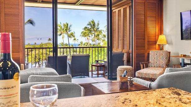 A balcony with a view of palm trees and the ocean, furnished with chairs and a table, and a bottle of wine on the table. - Top-Floor breathtaking views, close to beach! (Kamuela)