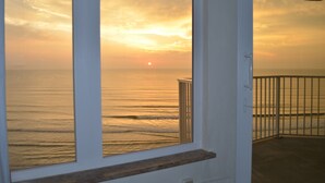A view through a window of a sunset over the ocean, with a railing and a door visible. - Updated Direct Oceanfront - 3 bedroom #1007; Beach Access and Heated Pool (Daytona Beach Shores)