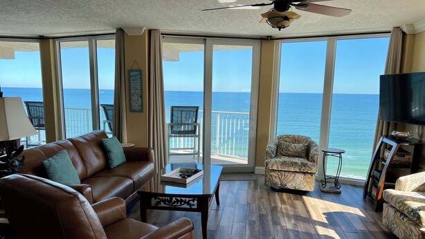 A spacious living room with a leather sofa, a small table, and a chair, all facing a large window with a view of the ocean. - Updated Direct Oceanfront - 3 bedroom #1007; Beach Access and Heated Pool (Daytona Beach Shores)